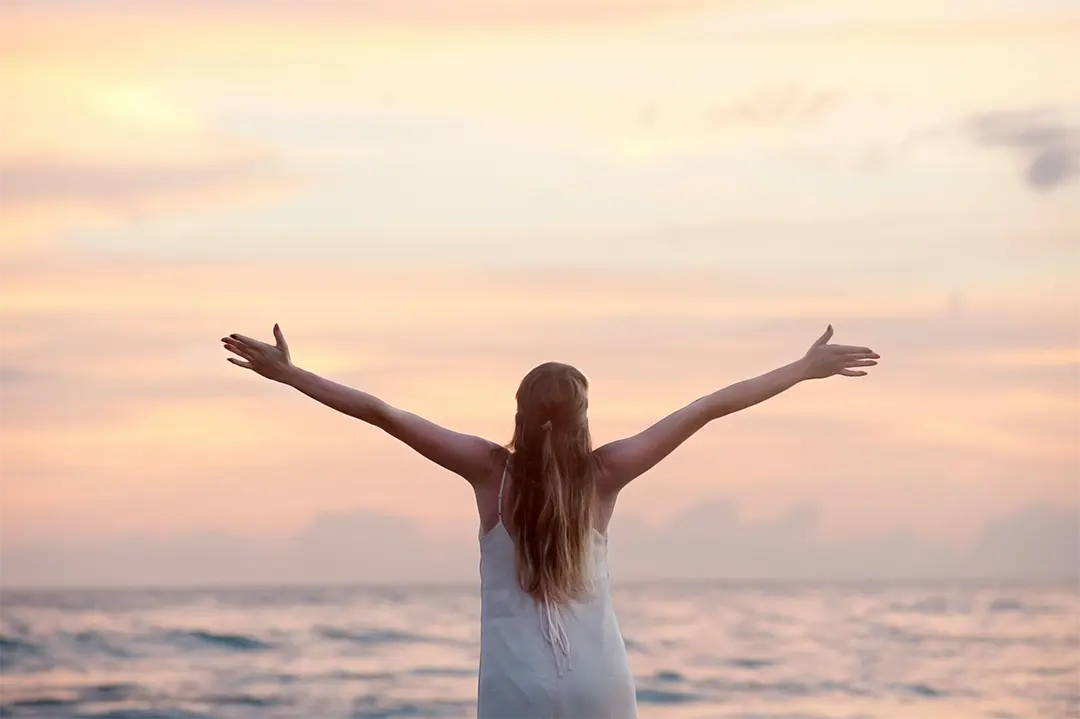 Home 6 woman with arms outstretched on a beach at sunset